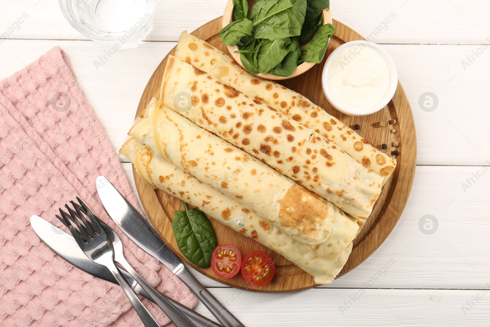 Photo of Tasty rolled crepes with cottage cheese and spinach served on white wooden table, flat lay