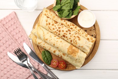 Photo of Tasty rolled crepes with cottage cheese and spinach served on white wooden table, flat lay