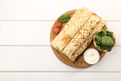 Photo of Tasty rolled crepes with cottage cheese and spinach served on white wooden table, top view. Space for text