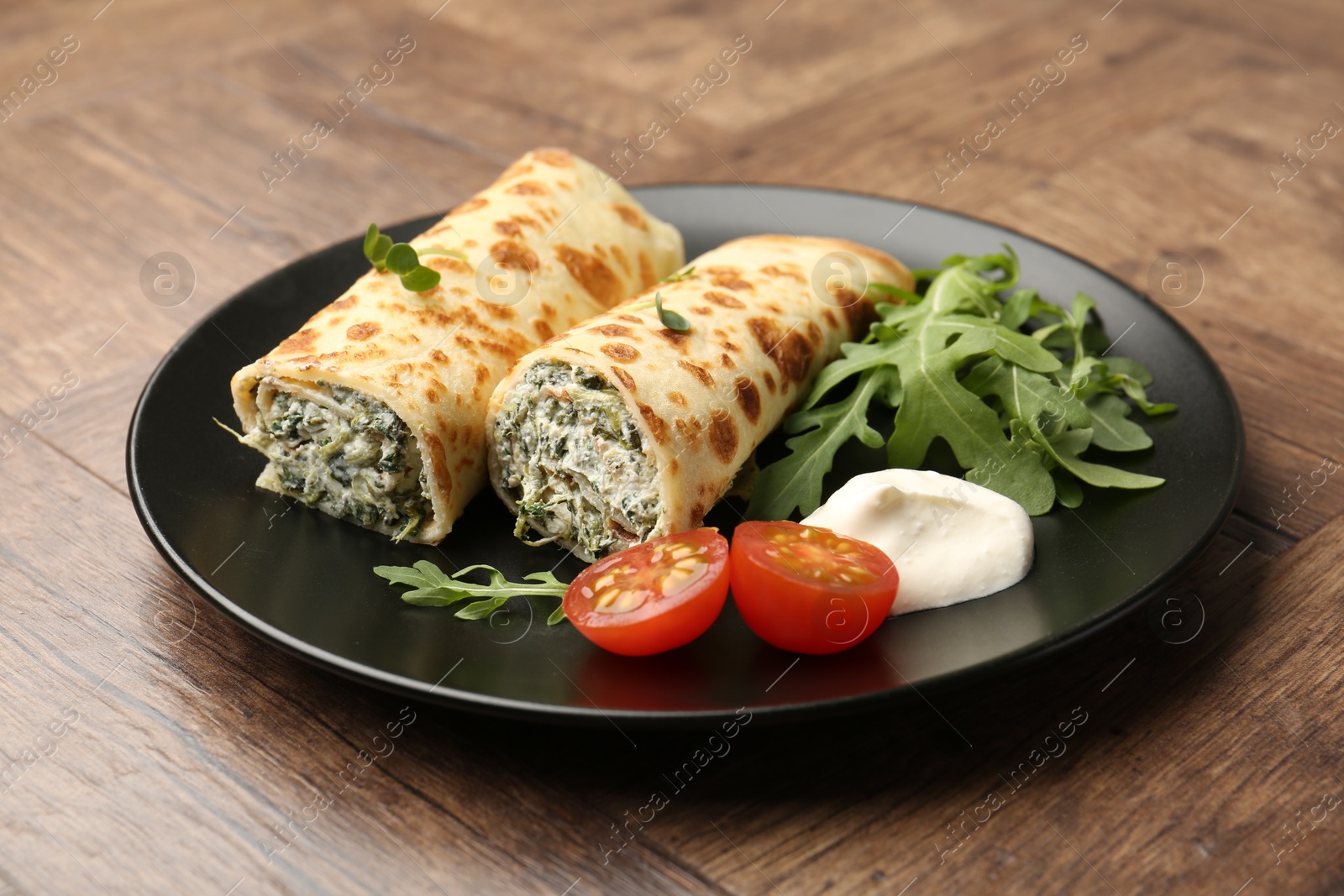 Photo of Tasty rolled crepes with cottage cheese and spinach served on wooden table, closeup