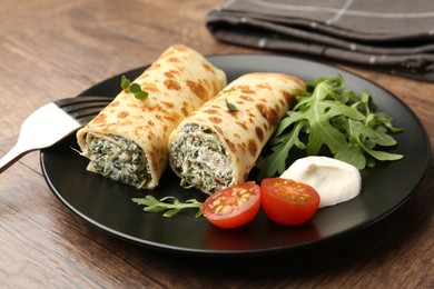 Photo of Tasty rolled crepes with cottage cheese and spinach served on wooden table, closeup