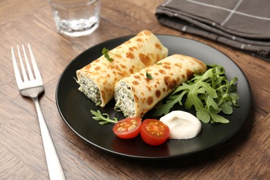 Photo of Tasty rolled crepes with cottage cheese and spinach served on wooden table, closeup