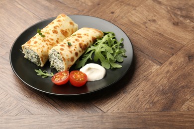 Photo of Tasty rolled crepes with cottage cheese and spinach served on wooden table, closeup. Space for text