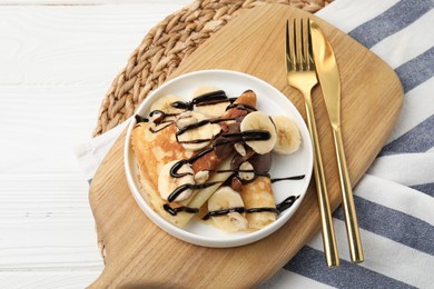 Photo of Delicious crepes with banana, nuts and chocolate sauce on white wooden table, above view