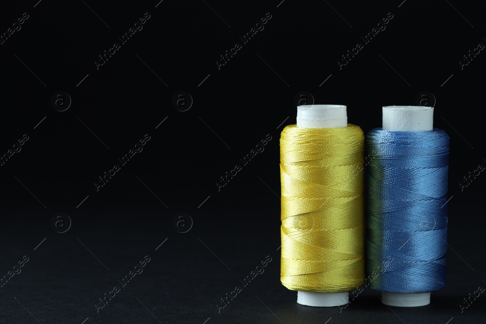 Photo of Spools of colorful sewing threads on black background, space for text