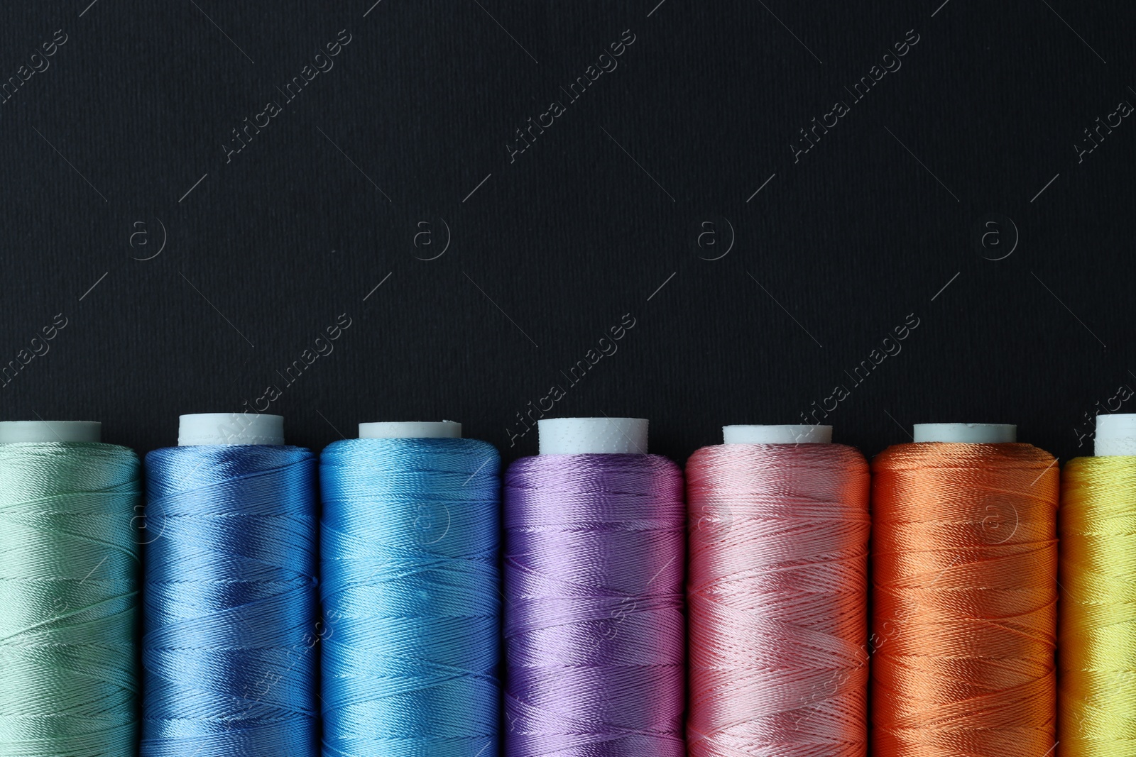 Photo of Spools of colorful sewing threads on black background, flat lay. Space for text