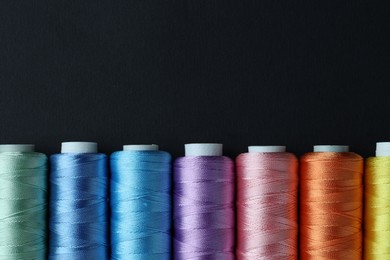 Photo of Spools of colorful sewing threads on black background, flat lay. Space for text