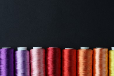 Photo of Spools of colorful sewing threads on black background, flat lay. Space for text