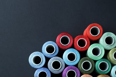 Photo of Spools of colorful sewing threads on black background, flat lay. Space for text