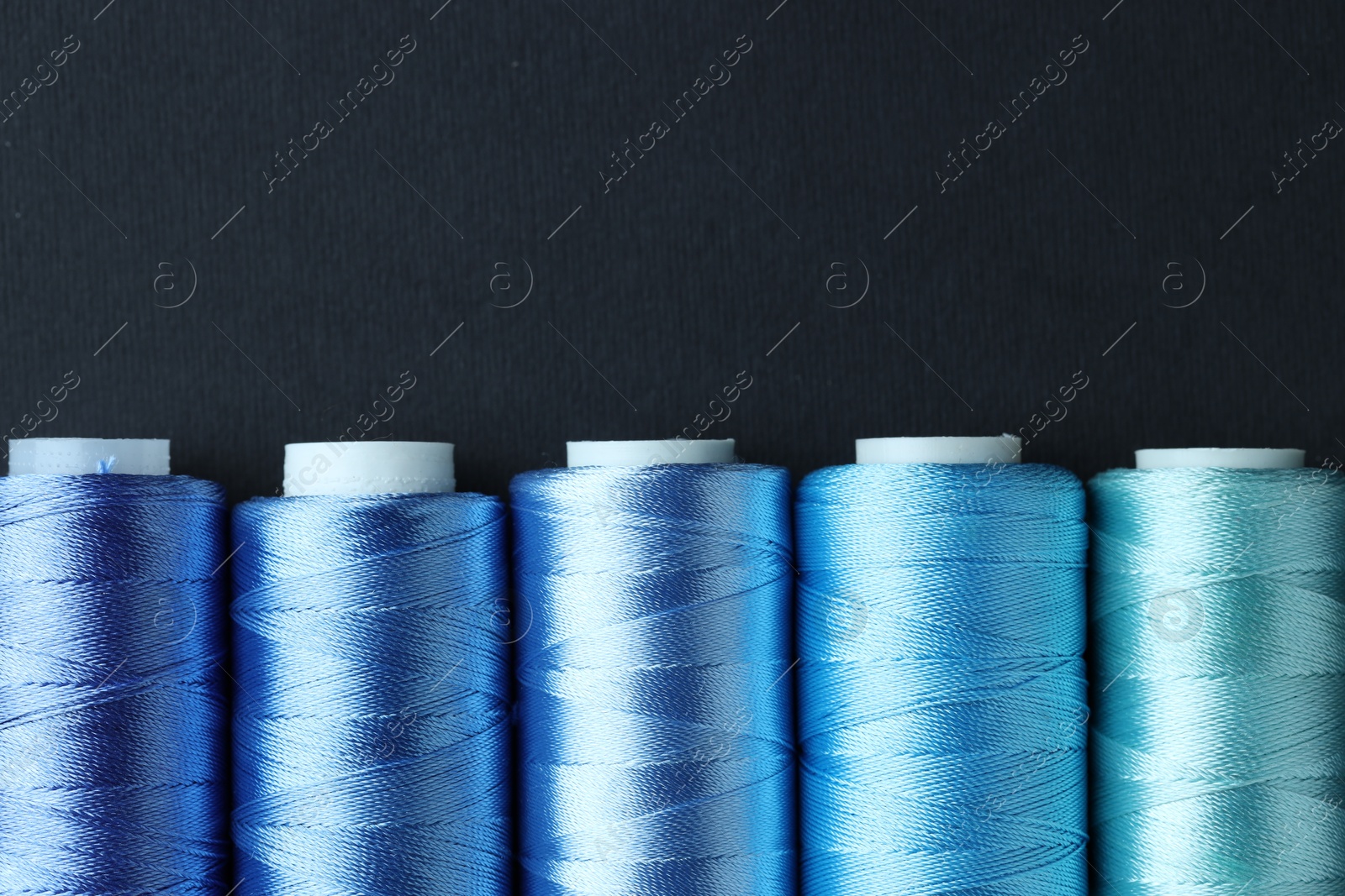 Photo of Spools of colorful sewing threads on black background, flat lay