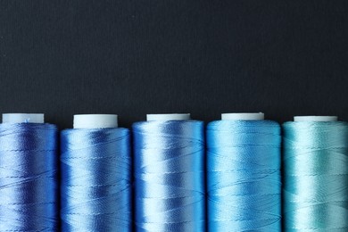 Photo of Spools of colorful sewing threads on black background, flat lay