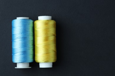 Photo of Spools of colorful sewing threads on black background, top view. Space for text