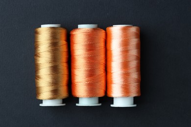 Photo of Spools of colorful sewing threads on black background, flat lay