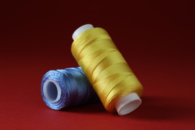 Photo of Spools of colorful sewing threads on red background, closeup