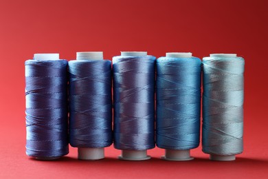 Photo of Spools of colorful sewing threads on red background