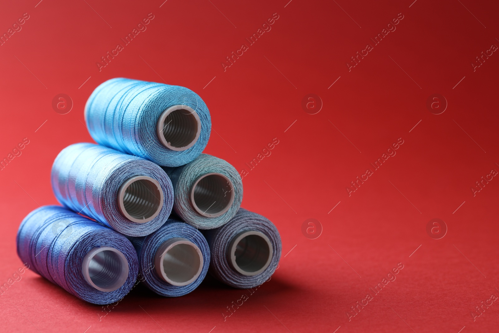 Photo of Spools of colorful sewing threads on red background, space for text