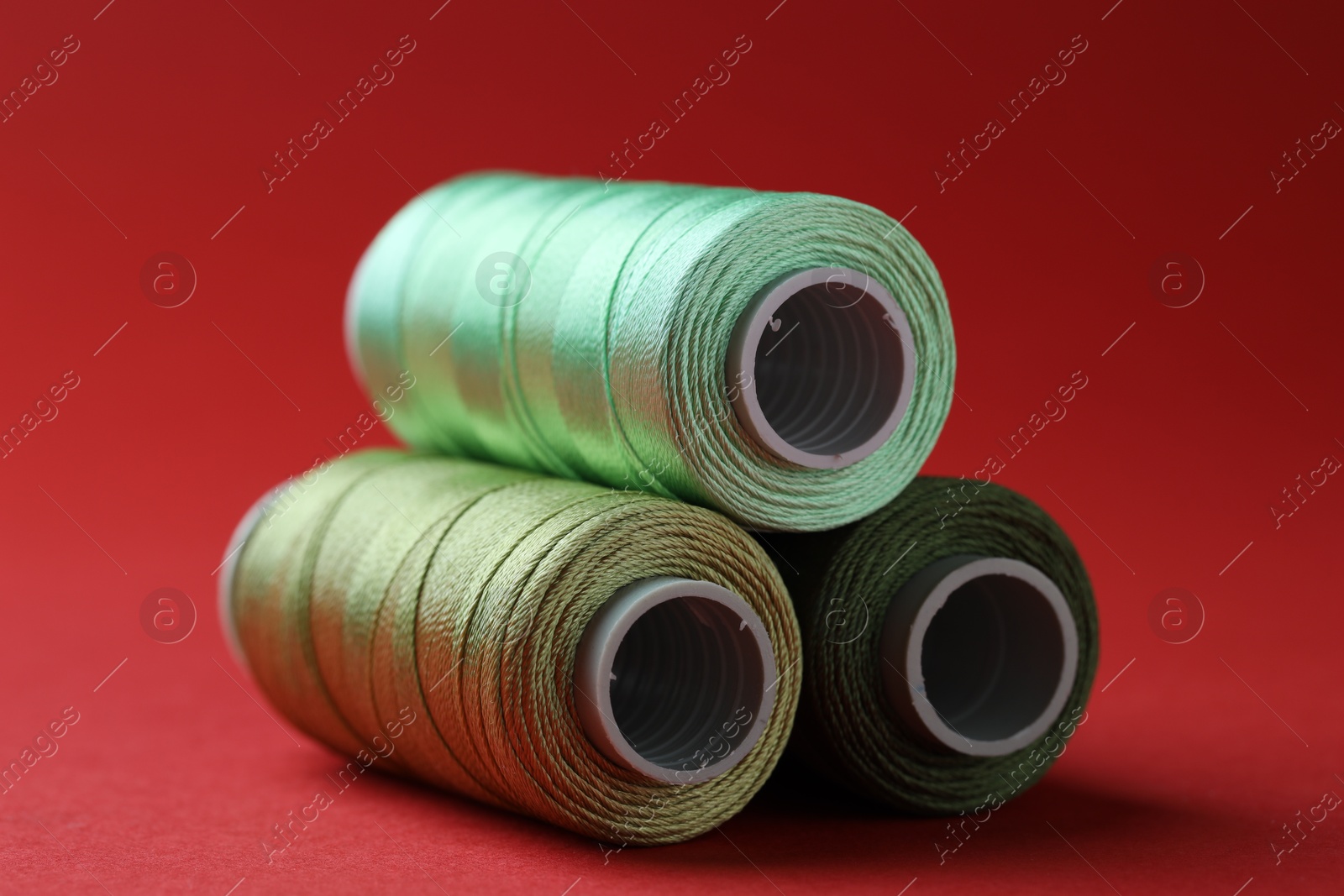 Photo of Spools of colorful sewing threads on red background, closeup