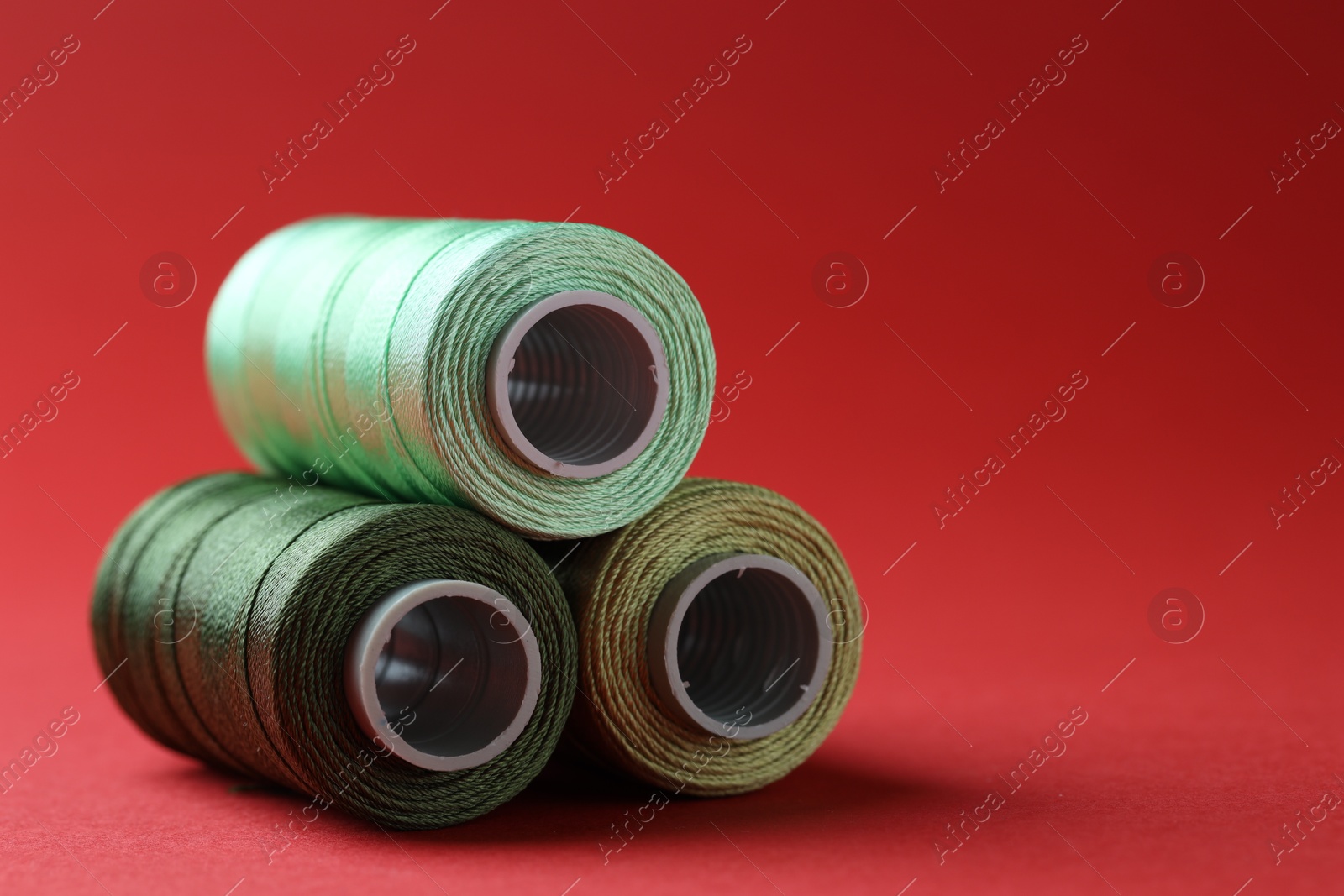 Photo of Spools of colorful sewing threads on red background, closeup. Space for text