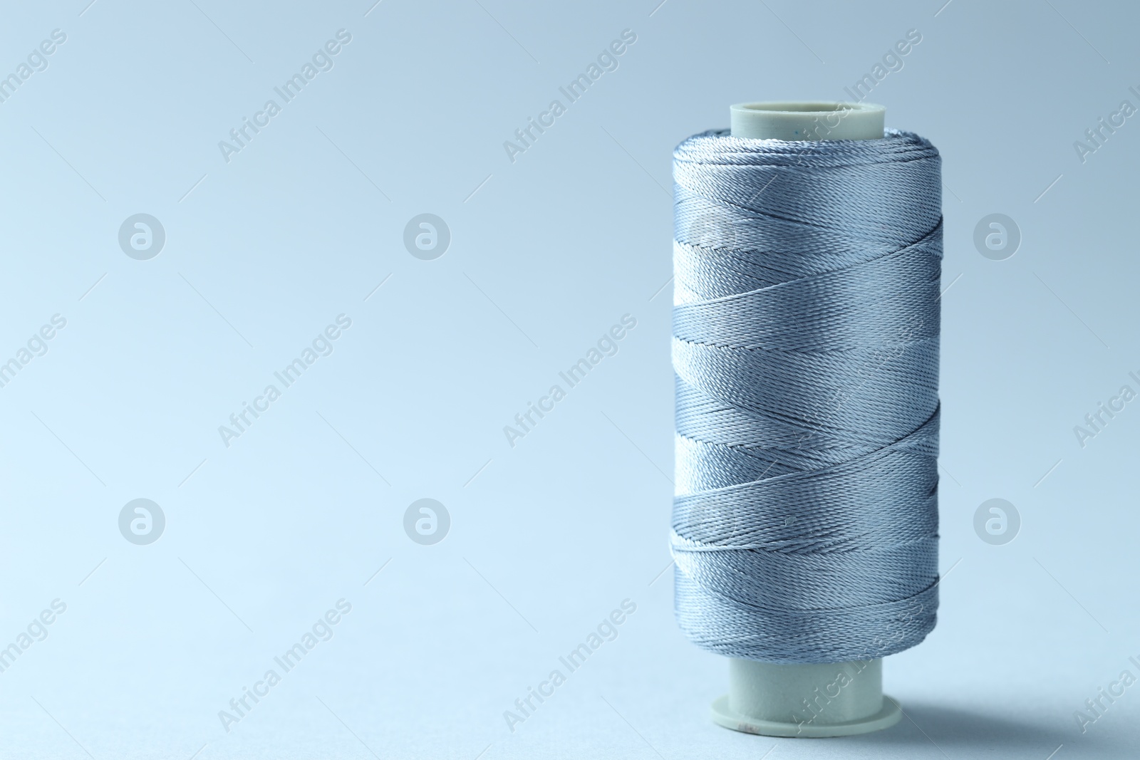 Photo of Spool of colorful sewing thread on light background, space for text