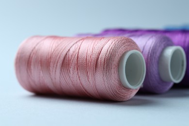 Photo of Spools of colorful sewing threads on light background, closeup