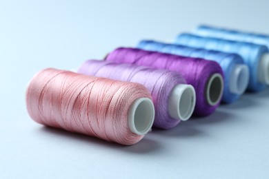 Photo of Spools of colorful sewing threads on light background, closeup