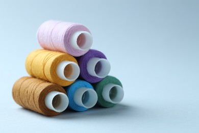 Photo of Spools of colorful sewing threads on light background, closeup. Space for text