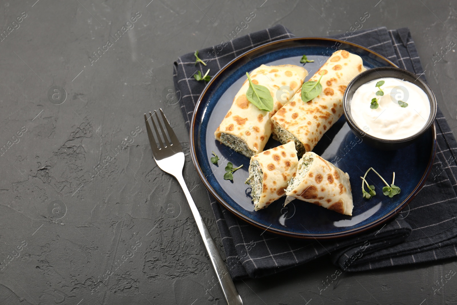 Photo of Delicious crepes with cottage cheese, spinach and sour cream served on black table. Space for text