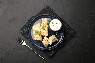 Photo of Delicious crepes with cottage cheese, spinach and sour cream served on black table, top view