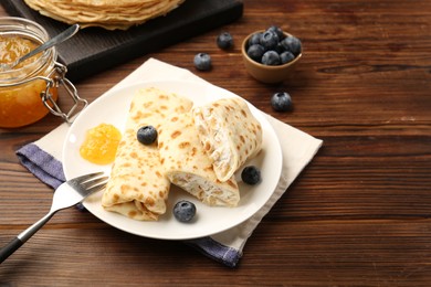 Photo of Delicious crepes with cottage cheese, jam and blueberries served on wooden table