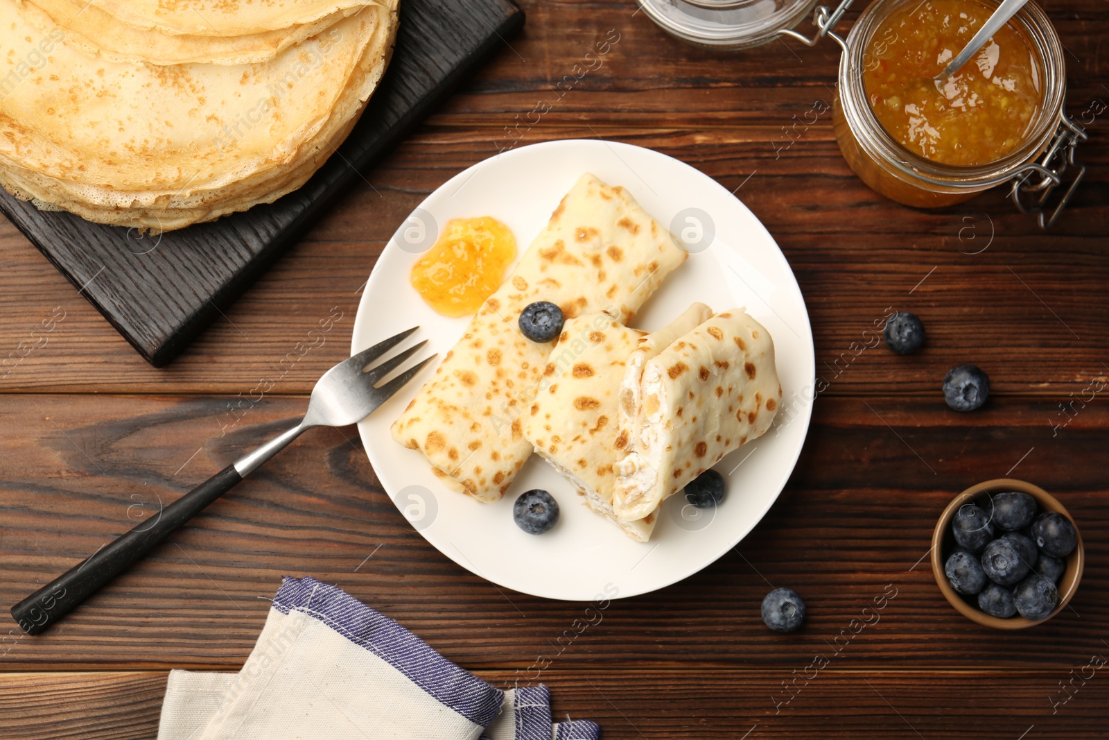 Photo of Delicious crepes with cottage cheese, jam and blueberries served on wooden table, flat lay