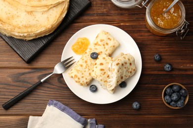 Photo of Delicious crepes with cottage cheese, jam and blueberries served on wooden table, flat lay