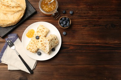 Photo of Delicious crepes with cottage cheese, jam and blueberries served on wooden table, flat lay. Space for text