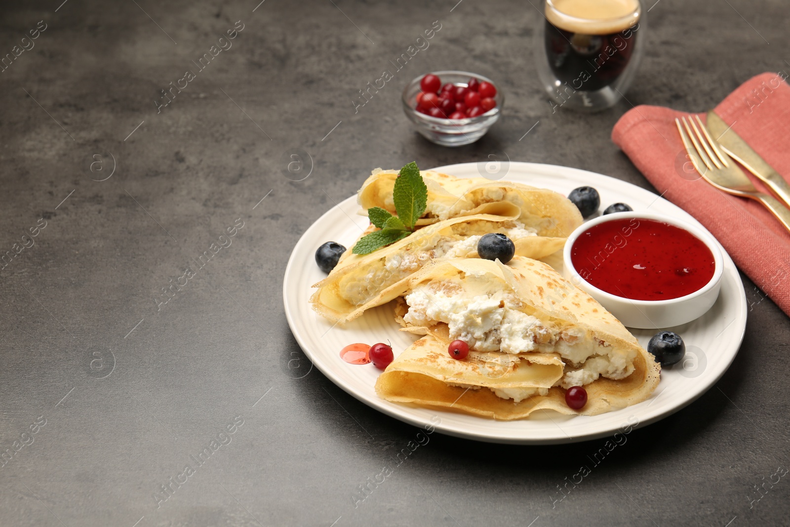 Photo of Delicious crepes with cottage cheese, jam, redcurrants and blueberries served on grey table. Space for text