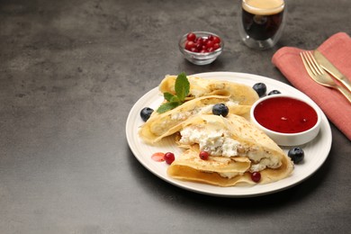 Photo of Delicious crepes with cottage cheese, jam, redcurrants and blueberries served on grey table. Space for text