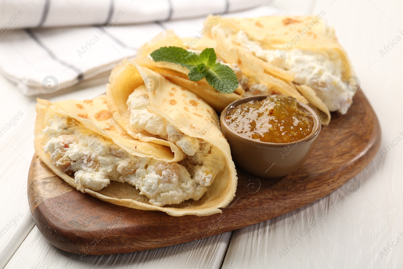 Photo of Delicious crepes with cottage cheese, jam and mint on white wooden table, closeup