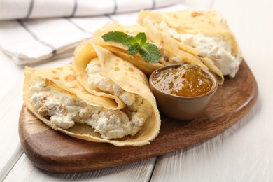 Photo of Delicious crepes with cottage cheese, jam and mint on white wooden table, closeup