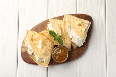 Photo of Delicious crepes with cottage cheese, jam and mint on white wooden table, top view