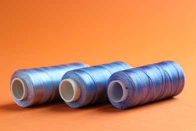 Photo of Spools of sewing threads on orange background, closeup