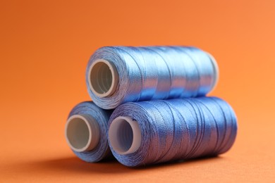 Photo of Spools of sewing threads on orange background, closeup