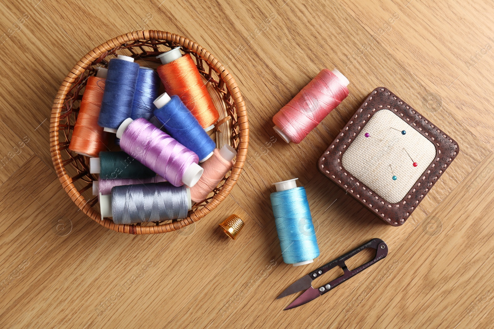 Photo of Sewing threads, snips, pincushion and thimble on wooden table, flat lay