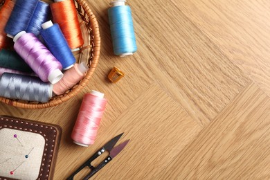 Photo of Sewing threads, snips, pincushion and thimble on wooden table, flat lay. Space for text