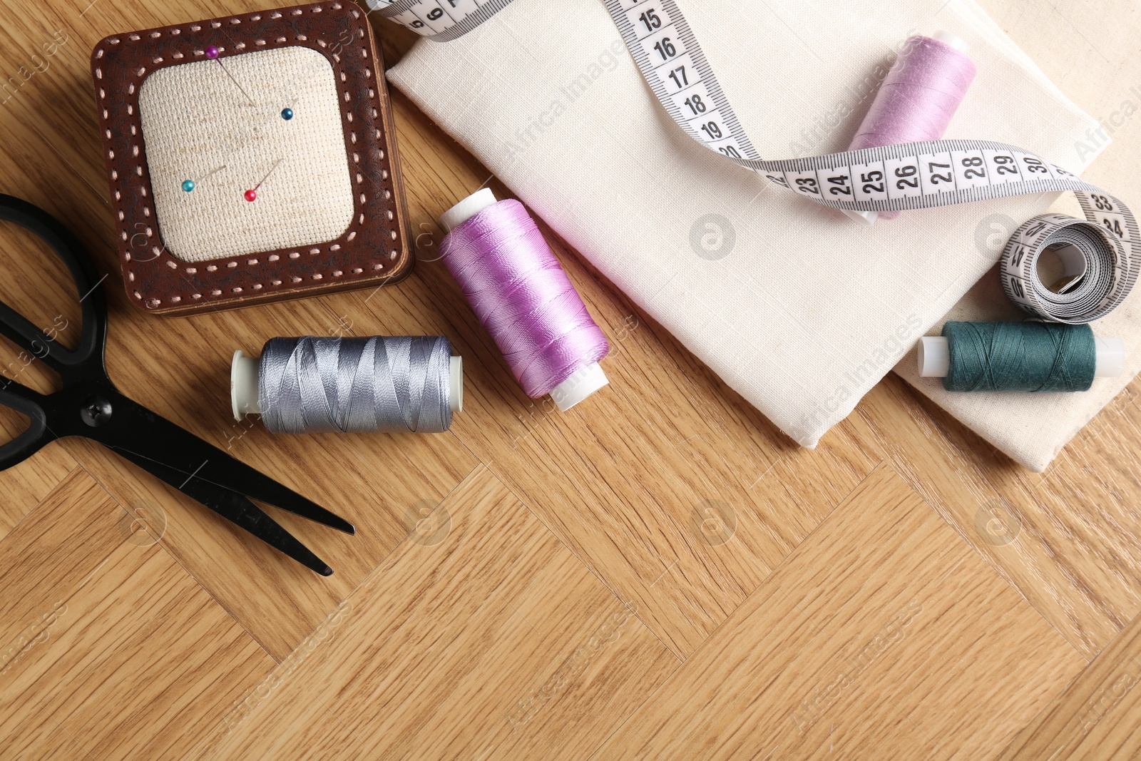 Photo of Sewing threads and other supplies on wooden table, flat lay. Space for text