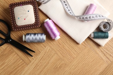 Photo of Sewing threads and other supplies on wooden table, flat lay. Space for text