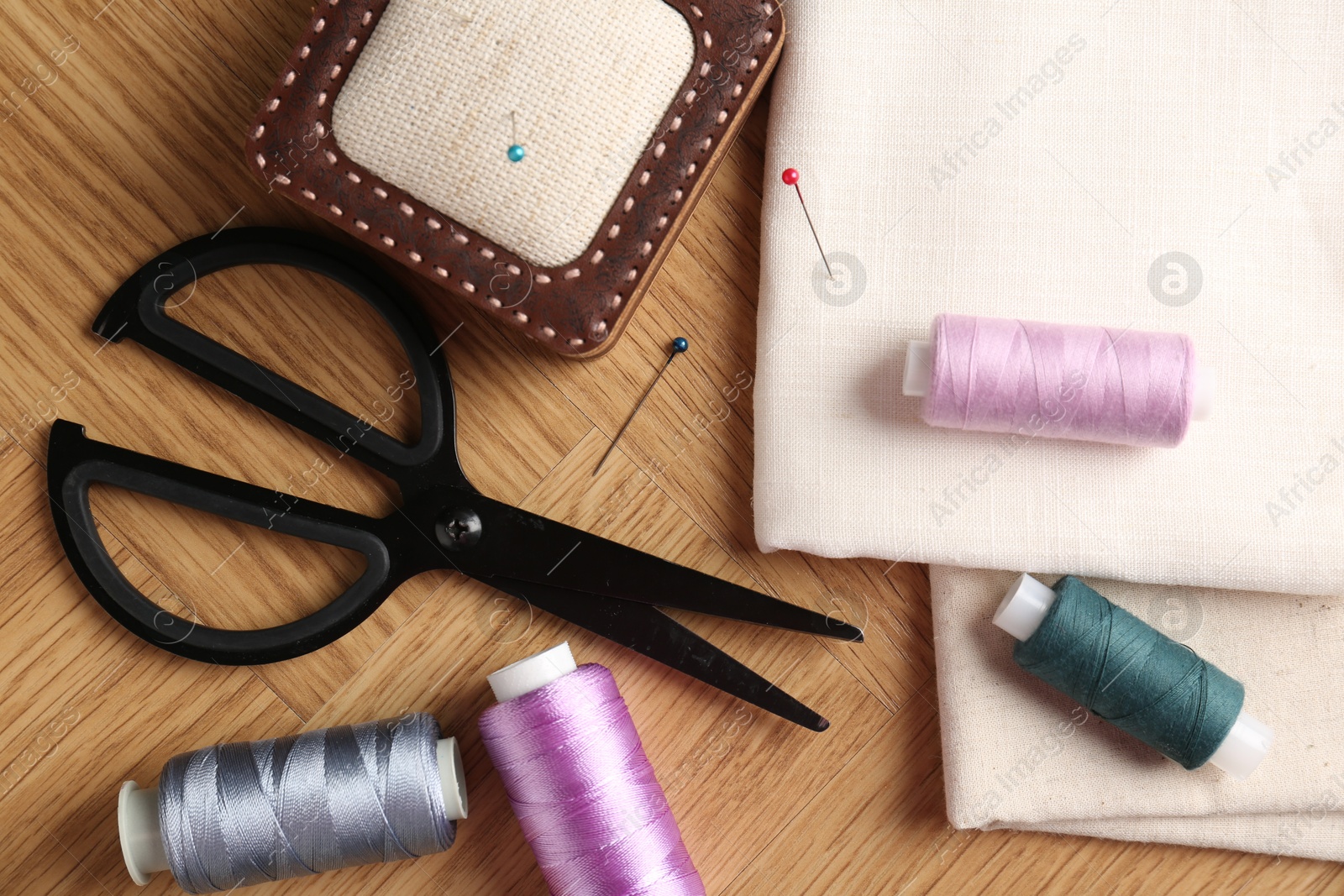 Photo of Sewing threads and other supplies on wooden table, flat lay