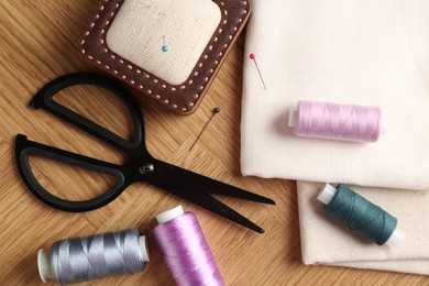 Photo of Sewing threads and other supplies on wooden table, flat lay