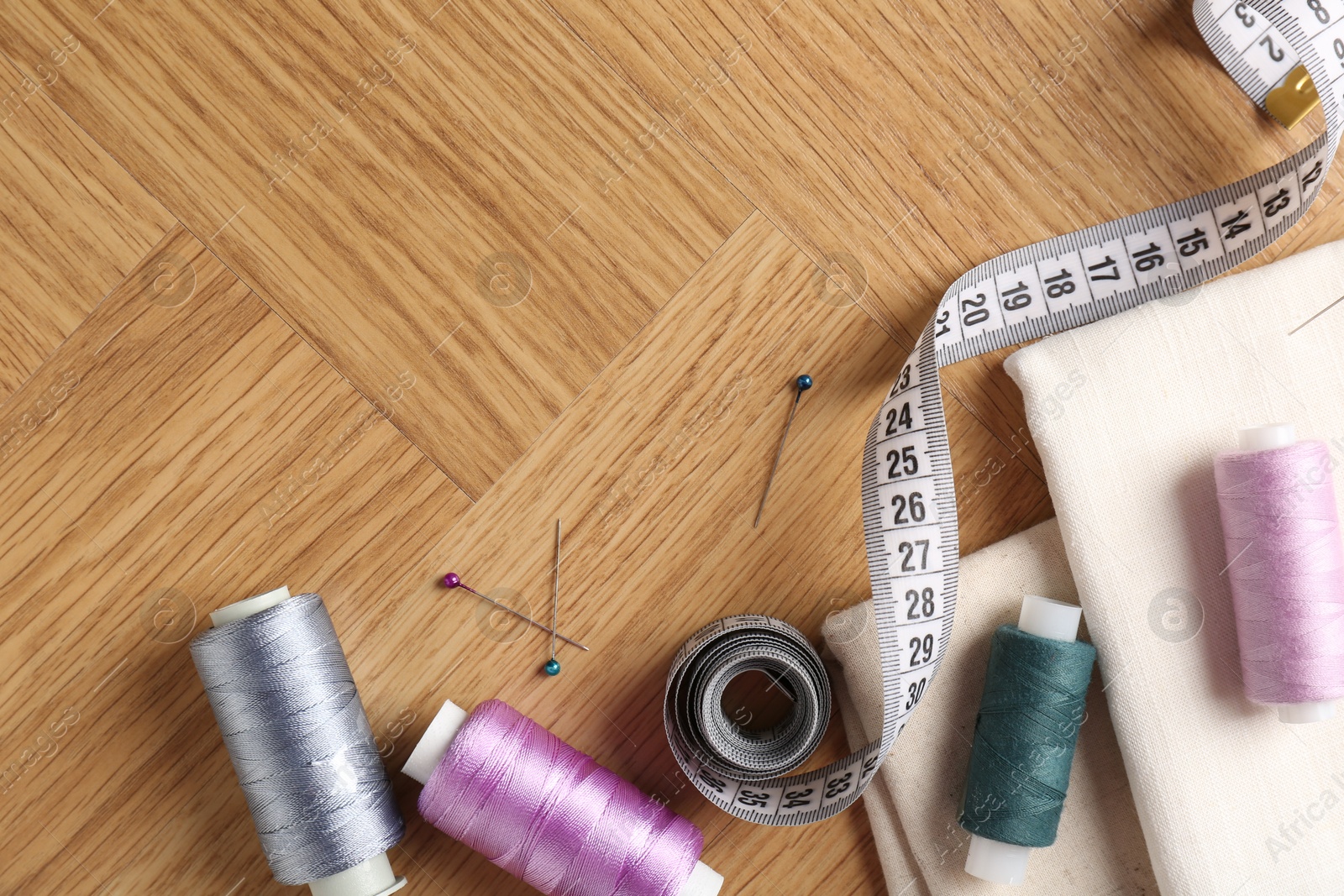 Photo of Sewing threads and other supplies on wooden table, flat lay. Space for text