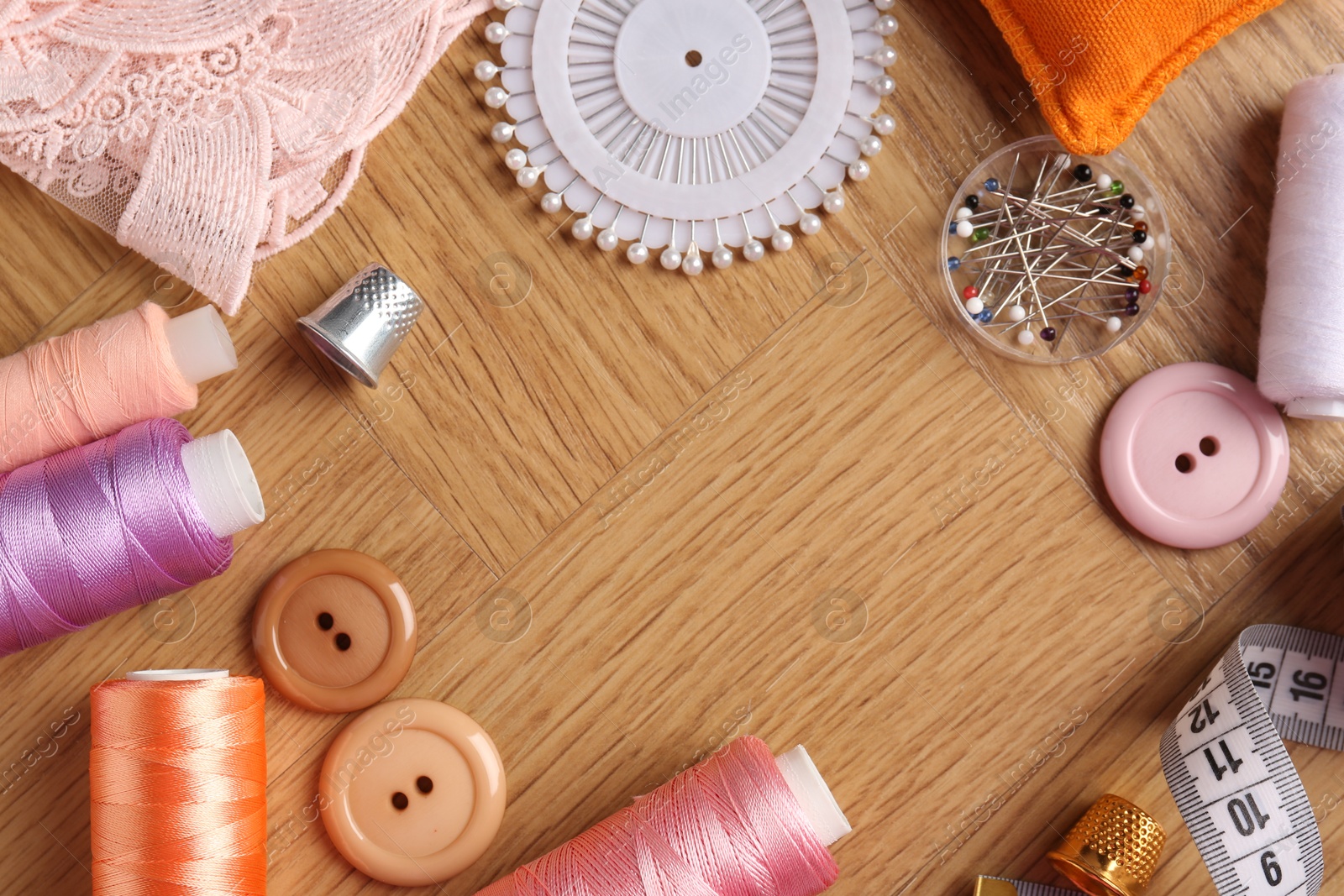 Photo of Frame of sewing threads and other supplies on wooden table, flat lay. Space for text