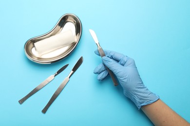 Doctor with surgical scalpels on light blue background, top view