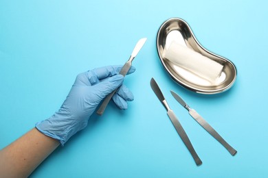 Photo of Doctor with surgical scalpels on light blue background, top view