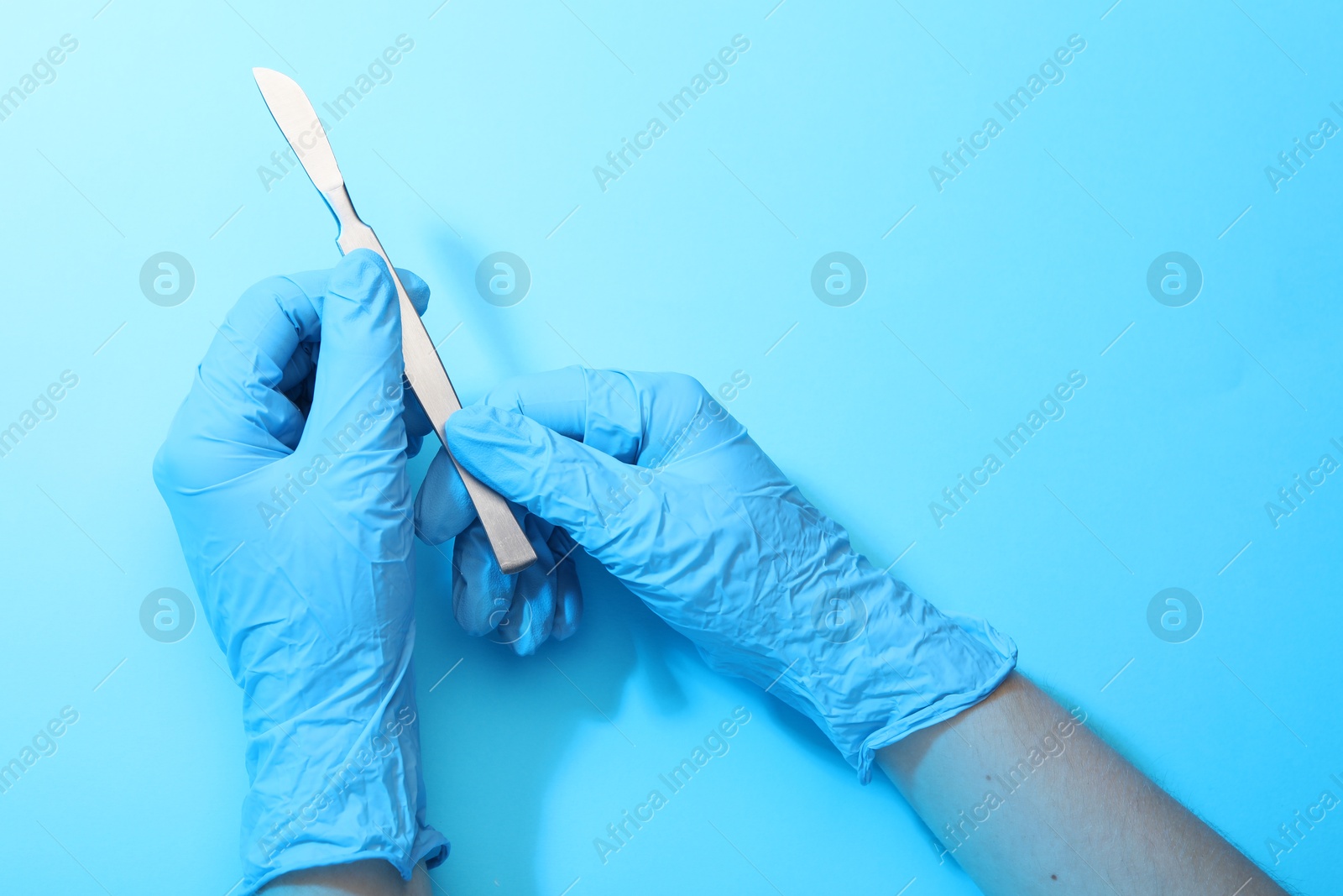 Photo of Doctor with surgical scalpel on light blue background, top view. Space for text